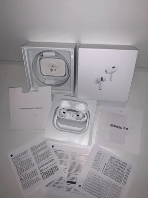 Apple AirPods Pro trådlösa hörlurar - Säljer ett par vita Apple AirPods Pro med laddningsetui och originaltillbehör. Hörlurarna har en stilren design, silikonproppar för bra passform och levereras med laddkabel och manualer. Perfekta för musik, samtal och träning tack vare brusreducering och smidig anslutning.