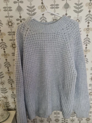 Ljusblå  stickad tröja - Mysig ljusblå stickad tröja med grov struktur och bred ribbad krage. Tröjan har lång ärm och avslappnad passform, perfekt för lager på lager. Inget synligt märke. Passar dig som gillar en chill och trendig look.