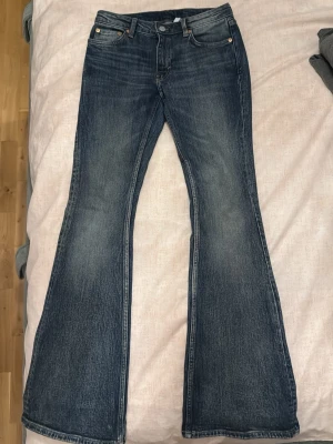 Weekday blå bootcut jeans lowwaist - Säljer ett par klassiska blå weekday jeans med bootcut passform. snygg slitning på. Perfekta för dig som gillar retrovibbar och vill ha ett par jeans med riktigt schysst siluett. 