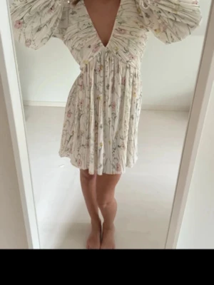 Blommig sommarklänning - Supersöt kortklänning med blommigt mönster i pastellfärger. Djup v-ringning och den är i ett lätt, luftigt material. 