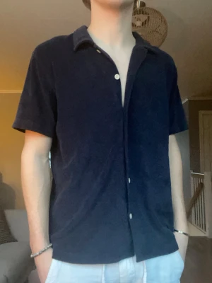 East West frotté skjorta – strl M - Riktigt snygg skjorta i frottématerial från East West. Perfekt som sommar-/semesterplagg eller till casual outfits. Mjuk, luftig och väldigt clean look.  Funkar sjukt bra öppen över linne/t-shirt eller knäppt.  Skick: Mycket bra skick Storlek: M Färg: Mörkblå  Pris: 349 kr