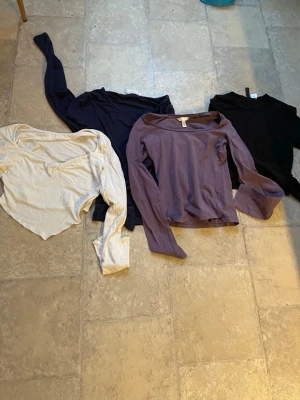 Fyra långärmade toppar i olika färger - Fyra långärmade toppar i svart, mörkblå, ljusbeige och lila. Alla har enkel design och rundad eller lätt v-ringad halsringning. Perfekta att matcha till olika outfits och stilar. går att köpa separat också!