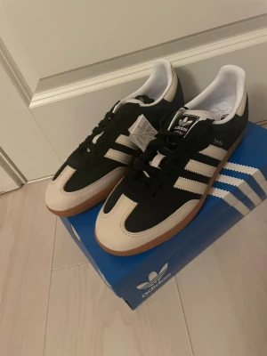 Adidas Samba sneakers svart/vit - Klassiska Adidas Samba sneakers i svart med vita detaljer och gummisula. Skorna har de ikoniska tre ränderna på sidan, snörning och rund tå. Perfekta för dig som gillar retrostil och streetwear.Helt nya.