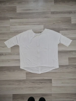 Vit topp med dragkedja bak - Vit, loose-fit topp med rund hals och korta ärmar. Toppen har en dekorativ dragkedja längs ryggen som ger en cool detalj. Perfekt att styla med jeans eller kjol.