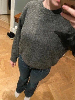 Grå stickad tröja från H&M - Mysig grå stickad tröja från H&M med rund halsringning och avslappnad passform. Perfekt att bära till jeans eller kjol. Tröjan har långa ärmar och är tillverkad i ett mjukt material som känns skönt mot huden.