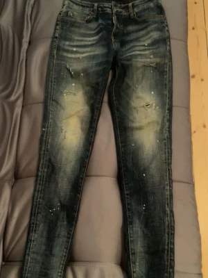  Disquerd Mörkblå slitna jeans med fit - Mörkblå jeans med skinny passform och slitna detaljer framtill. Jeansen har ljusa partier och små färgstänk för en cool, använd look. Klassisk femficksmodell med dragkedja och knapp. Perfekta för dig som gillar en trendig streetstil.