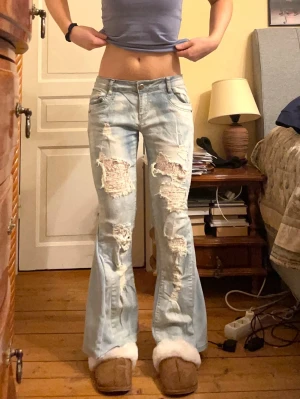 Lågmidjade jeans med spets slitningar - Säljer dessa så snygga och unika jeans! De är i en ljusblå färg, är omsydda till bootcut och har insytt spetstyg under slitningarna. Midjemått 39 cm och innerbenslängd 70 cm. Säljer liknande jeans i min profil 💕💕