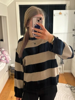 Beige och svart randig stickad tröja - Stickad tröja med breda beige och svarta ränder. Tröjan har rund halsringning och långa ärmar. Perfekt för en avslappnad och trendig look. Är i storlek S o har inga skador 