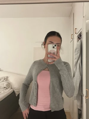 Grå cropped kofta med rund hals - Snygg grå kofta i cropped modell med rund halsringning och knäppning framtill. Perfekt att styla över ett linne eller t-shirt. Mjuk och tunn stickning som passar året runt.