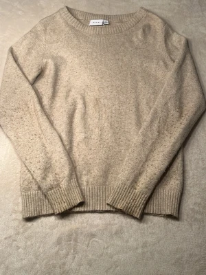 Beige stickad tröja - Mysig beige stickad tröja med rund halsringning och ribbade muddar vid ärmslut och nederkant. Perfekt för lager-på-lager och enkel att matcha med andra plagg.