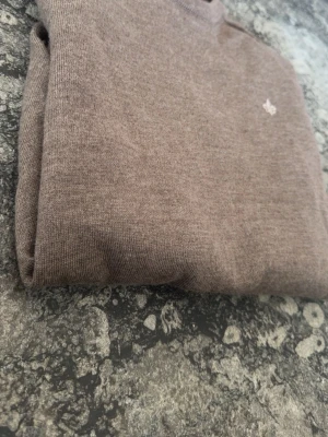 Brun merinoullströja från Morris - Snygg brun stickad tröja från Morris i 100% merinoull. Klassisk rund halsringning och diskret broderad logga på bröstet. Perfekt för dig som gillar stilrena och bekväma plagg i högkvalitativt material. Tröjan är lite liten, så skulle säga att tröjan är runt S.