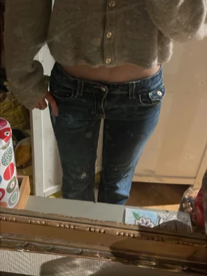 Blå lågmidjade bootcut jeans - Snygga blå jeans med låg midja och bootcut passform. Jeansen har dekorativa fickor med knappdetaljer bak och klassisk jeanslook med slitningar. Perfekta för dig som gillar en retro vibe och vill sticka ut. Använd några gånger! Storlek 170/S:)) 