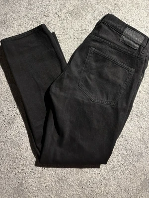 Svarta jeans från Lager 157 - Säljer ett par svarta jeans från Lager 157 med raka ben och klassisk femficksdesign. Jeansen har en enkel look utan slitningar och är tillverkade i mjuk bomull med lite stretch för extra komfort. Nypris 200 kr!