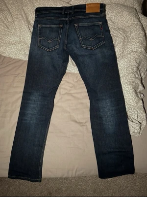 Mörkblå replay jeans - Säljer ett par mörkblå Replay jeans med klassisk femficksdesign och raka ben. Jeansen har snygga slitningar framtill och kontrastsömmar. Tillverkade i slitstarkt denim med läderpatch bak i midjan. Perfekta för en avslappnad och trendig look.