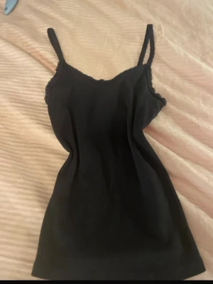 Svart ribbad linnetopp - Snygg svart ribbad linnetopp med smala axelband och lätt vågig kant upptill. Perfekt att styla till jeans eller kjol för en enkel och clean look.