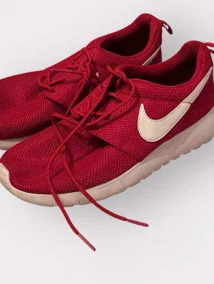 Röda Nike sneakers med vit sula - Snygga röda Nike sneakers med vit sula och vit swoosh på sidan. Skorna har snörning och är tillverkade i ett ventilerande meshmaterial som ger en sportig look. Perfekta för dig som vill ha en stilren och bekväm sneaker till vardags.