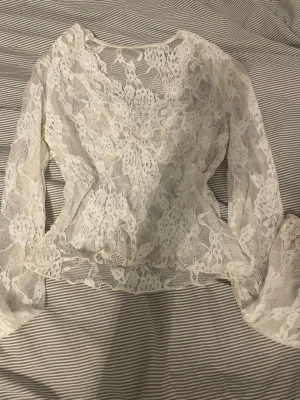Vit spetsblus med v-ringning - Säljer en superfin vit blus i spets med v-ringad hals och långa ärmar. Blusen har ett romantiskt mönster och är genombruten i materialet vilket ger en luftig och elegant känsla. Perfekt att styla med jeans eller kjol för en trendig look.