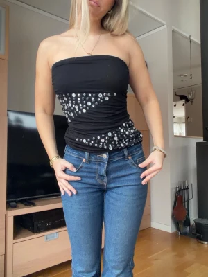 Svart tubtopp med silverprickar - Säljer en svart axelbandslös tubtopp med glittriga silverprickar i diagonala mönster. Toppen är tight och har en bandeauform som sitter snyggt på kroppen. Perfekt för dig som vill sticka ut lite extra.