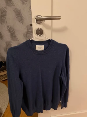 Blå stickad tröja från NN07 - Mörkblå stickad tröja från NN07 med rund halsringning och ribbade muddar vid ärmslut och nederkant. Enkel och stilren design som passar perfekt till jeans eller chinos. Nypris 1500