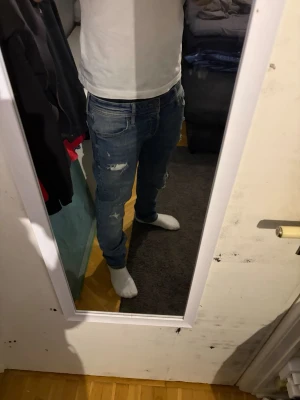 Blå jack and jones jeans herr - Säljer ett par blå jack ans jones jeans med slitningar och hål på benen för en trendig look. Jeansen har normal passform, klassisk femficksdesign och är tillverkade i bomull med lite stretch. Perfekta för dig som gillar en avslappnad men snygg stil. w32 l34 hål vid knän