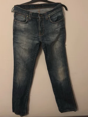 Blå jeans från Nudie Jeans - Snygga blå jeans från Nudie Jeans med klassisk femficksdesign och orangea sömmar på bakfickorna. Perfekta för en avslappnad och trendig look. Ett hål på baksidan (se bild 3) som jag själv tycker ger en snyggare look