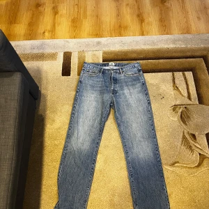 Blå jeans från 157 Seattle W31 L34 - Snygga blå jeans från 157 Seattle i klassisk tvätt. Modellen har raka ben och normal passform, med fem fickor och gylf med dragkedja. Perfekta för dig som gillar en enkel och tidlös look. Storlek W31 L34.