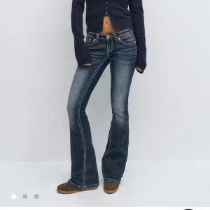 Blå bootcut jeans med kontrastsömmar i Tall - Snygga blå bootcut jeans med markerade kontrastsömmar och låg midja. Jeansen har klassisk femficksdesign och en lätt tvättad look med slitningar på låren. Perfekta för dig som gillar en retro vibe och vill ha ett par jeans som sticker ut. Jensen är i modellen Tall 