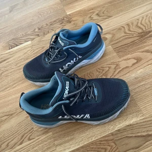 Hoka One One Bondi 7 sneakers blå - Säljer ett par Hoka One One Bondi 7 sneakers i mörkblått med ljusblå detaljer och vit sula. Skorna har snörning, mesh-ovandel och extra tjock, dämpad sula för maxad komfort. Perfekta för dig som gillar att springa eller promenera långt/ jobbskor