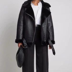 PU-jacka från NA-KD - Säljer en svart pälsjacka med skinnstruktur och mjuk päls på insidan och kragen. Jackan har en bred krage, sned dragkedja och bälte vid midjan och halsen. Passformen är loose och jackan har långa ärmar med pälsdetaljer vid muddar och nederkant. Nypris 1099kr