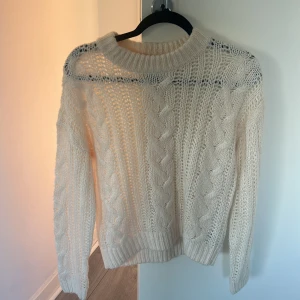 Beige stickad tröja med flätmönster - Säljer en beige stickad tröja med snyggt flätmönster och grov struktur. Tröjan har rund hals och långa ärmar, perfekt för att hålla sig varm och se chill ut under kyliga dagar. Passar dig som gillar klassisk stil med en modern twist.