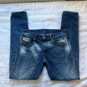 Blå Diesel jeans W30 med slitningar - Säljer ett par blå jeans från Diesel med snygga slitningar och tvättade detaljer. Klassisk femficksmodell med Diesel Industry-märke på myntfickan och patch bak. Jeansen är raka/slim i modellen och tillverkade i bomull med lite stretch för skön passform.