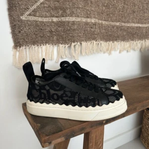 Svarta sneakers från Chloé med spets - Snygga svarta sneakers från Chloé med vit sula och coola spetsdetaljer. Skorna har tydlig logga baktill och på sidorna, snörning och vågig kant längs sulan. Ovandelen är i mesh och spets för en unik look. Perfekta för dig som vill sticka ut med stil. I super duper bra skick , storlek 37 men passar även 36🥰