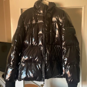 Calvin klein jeans jacka - Säljer en svart, glansig pufferjacka från Calvin Klein Jeans med huva och tydlig CK-logga på ryggen och ärmen. Jackan har quiltad design, dragkedja framtill och breda muddar vid ärmslut. Perfekt för kalla dagar och är snygg för alla olika stilar! Använt den en vinter! (Kan diskutera pris)