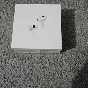 AirPods Pro (2nd generation) - Säljer ett par Apple AirPods Pro (2nd generation) i originalförpackning. Komplett med laddningsetui och kabel, tillverkade 2023. Produkten ser ut att vara i mycket gott skick utan synliga defekter eller slitage. Perfekt för dig som vill ha trådlösa hörlurar med aktiv brusreducering.