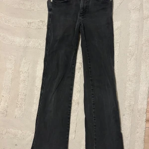 Mörkgrå bootcut jeans  - Mörkgrå jeans från 157 med bootcut-modell och klassisk femficksdesign. Snygga bakfickor med lock och silverfärgade knappar. Jeansen har låg midja och är tillverkade i ett stretchigt bomullsmaterial. Två små vita fläckar finns på låret. 