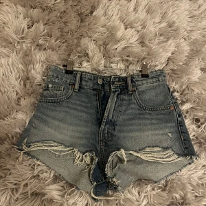 Supersöta  jeansshorts från Zara - Snygga blå jeansshorts från Zara med råa, fransiga kanter. Shortsen har slitna detaljer framtill och klassiska fem fickor. Perfekta för sommaren och ger en cool, avslappnad vibe.