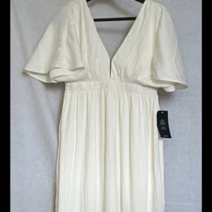 Vit långklänning från NA-KD, stl 36 - Säljer en flowy långklänning från NA-KD i offwhite. Klänningen har djup v-ringning, vida korta ärmar och markerad midja. Materialet är lätt och ger ett luftigt intryck. Perfekt för sommarens alla tillfällen!