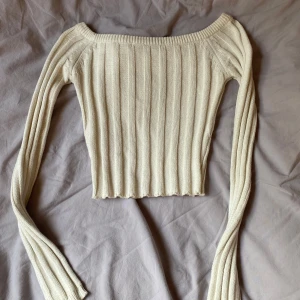Ribbad offshoulder topp från NA-KD - Säljer en krämvit ribbad stickad topp från NA-KD i storlek XXS. Toppen har offshoulder-modell, långa ärmar och croppad passform. Perfekt för dig som gillar en enkel men snygg stil.