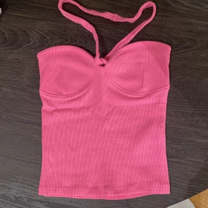 Rosa ribbad topp från Gina Tricot - Säljer en rosa ribbad topp från Gina Tricot i storlek XXS. Toppen har en croppad passform, bygelinspirerad kupa och smala axelband som kan knytas. 