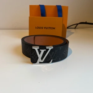 Svart bälte med silvrigt spänne - Snyggt svart bälte med klassiskt monogrammönster och silver på spännet. Bältet är gjort i skinn med bruna insidor och exklusiv känsla. Perfekt accessoar för att lyfta din outfit med en lyxig touch. Med följer box, påse och kvitto. Priset kan diskuteras vid snabb affär✅