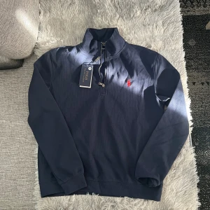 Marinblå half zip från Polo Ralph Lauren - Snygg marinblå långärmad tröja från Polo Ralph Lauren med half zip och klassisk röd broderad logga på bröstet. Tröjan är i bomull och har ribbade muddar för en clean look. Perfekt för dig som gillar stilrena och tidlösa plagg. Sprillans ny också🙌