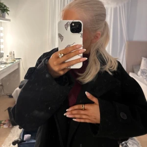 Svart kappa från Design by Si - Säljer en svart kappa från Design by Si med stora knappar, bred krage och rejäla fickor. Jackan har långa ärmar med knappdetalj vid mudden och är gjord i ett ulligt material. Perfekt för dig som gillar en klassisk och stilren look. Pris går alltid att diskutera!!🤍🤍