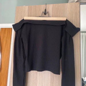 Svart ribbad offshoulder topp H&M - Svart ribbad offshoulder topp från H&M Divided. Toppen har långa ärmar och croppad passform, perfekt för en trendig look. Tillverkad i mjuk bomullsblandning med stretch för extra komfort. Enkel att matcha med både jeans och kjol.