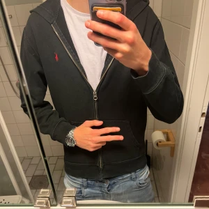 Ralph lauren zip  - Svart hoodie från Polo Ralph Lauren i storlek XL med dragkedja och huva. Klassisk design med röd broderad logga på bröstet och känguruficka framtill. Perfekt för en chill och stilren look.