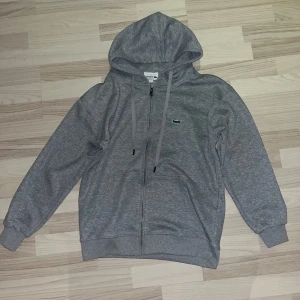 Lacoste zipper grå - Säljer en grå hoodie från Lacoste med klassisk krokodillogga på bröstet. knappast använda priset kan diskuteras vid snabb affär och har ni några frågor äre bara att skriva.