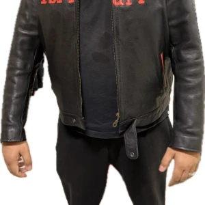 Ferrari Michael Schumacher F1 World Champion 2004 – Äkta Skinnjacka (3XL) - Sällsynt Ferrari Michael Schumacher F1 World Champion 2004 skinnjacka i storlek 3XL – för samlare och riktiga F1-fans. 	•	Äkta skinn (märkning: “Real Leather”) 	•	Broderade loggor: Ferrari, Michael Schumacher F1 World Champion, samt 2004-mästerskapets symbol 	•	Svart med röd brodyr och detaljer 	•	Dragkedja fram och justerbart midjespänne  Jackan är i mycket fint vintage-skick och ett måste för dig som älskar Ferrari eller Formel 1-historia. Passar perfekt som samlarobjekt eller statement-piece.