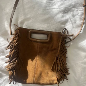 Brun mocka väska från Maje - Snygg brun axelväska från Maje i mocka med coola fransdetaljer på sidorna och ett stilrent handtag upptill. Väskan har en justerbar axelrem. 💞💞 Lite använd