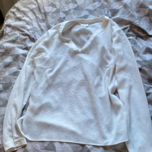 Vit v-ringad tröja från Vila - Säljer en stilren vit långärmad tröja från Vila med v-ringning. Tröjan har en lätt ribbad struktur och är i ett mjukt material som känns skönt mot huden. Perfekt för dig som gillar en clean och enkel look.