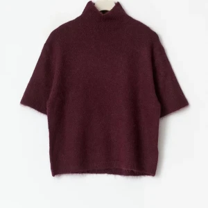 Vinröd stickad polotröja med kort ärm - Vinröd stickad polotröja med korta ärmar och hög krage. Tröjan har en loose passform och är tillverkad i ett mjukt, fluffigt material som känns lyxigt. Perfekt för lager-på-lager och ger en cool vibe till din outfit.