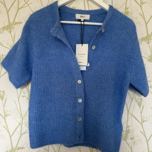 Blå kofta i ullmix från Gina Tricot - Superfin ljusblå kofta från Gina Tricot i mjuk ullblandning. Kortärmad modell med ribbad struktur och snygga knappar framtill. Perfekt att slänga över en topp för en chill look. Klassisk krage och skön passform.